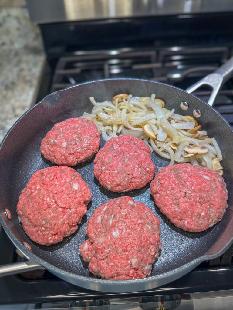 hamburger patties and onions in the skillet